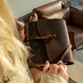 Person holding a brown leather bag with a blurred background