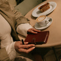 Person sitting at a table with a coffee and pastry, holding a small journal.